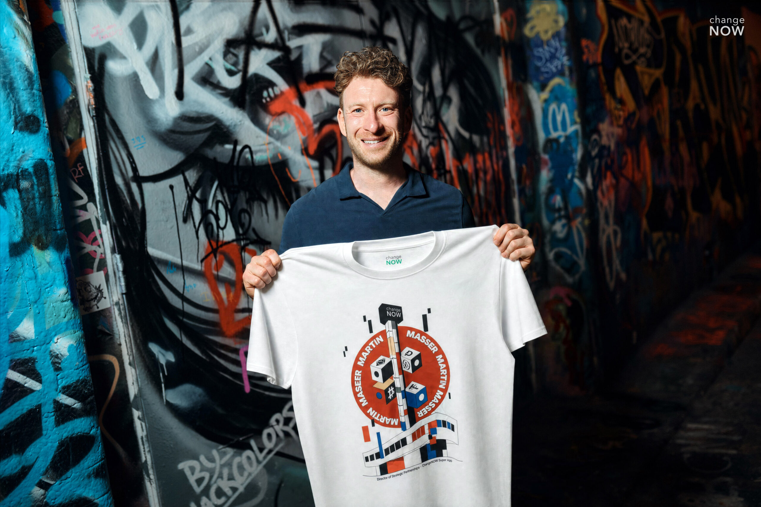 Martin Masser, ChangeNOW’s Director of Strategic Partnerships, holds a branded T-shirt in a graffiti-covered London passage.